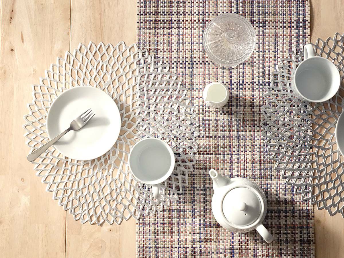 発色のよいシルバーでダリアの花を模ったのチルウィッチの円形ランチョンマットとマルチカラーの平織りのテーブルランナーでコーディネートした食卓