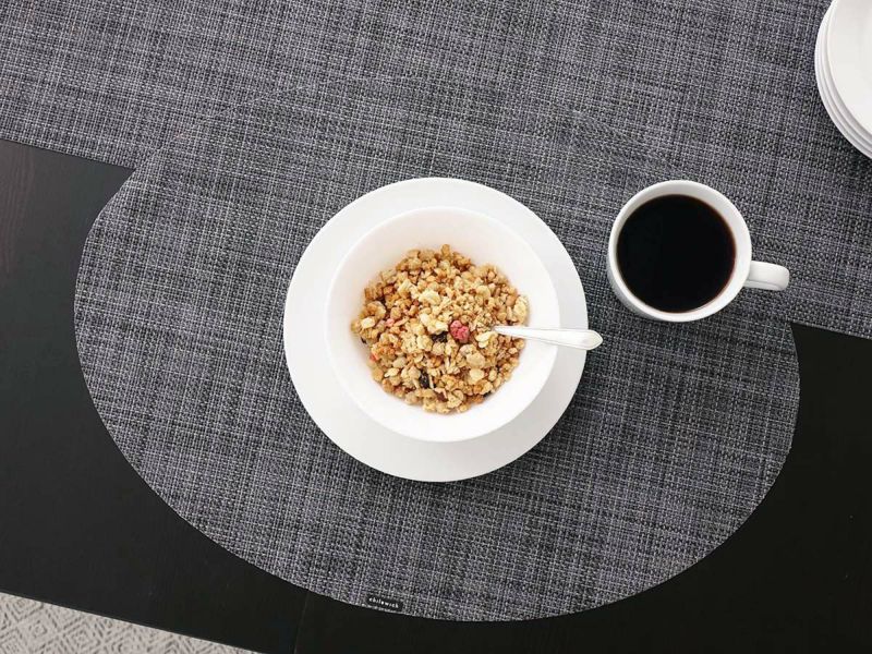 黒のテーブルに合わせた平織りの楕円形のダークグレイのチルウィッチのランチョンマット